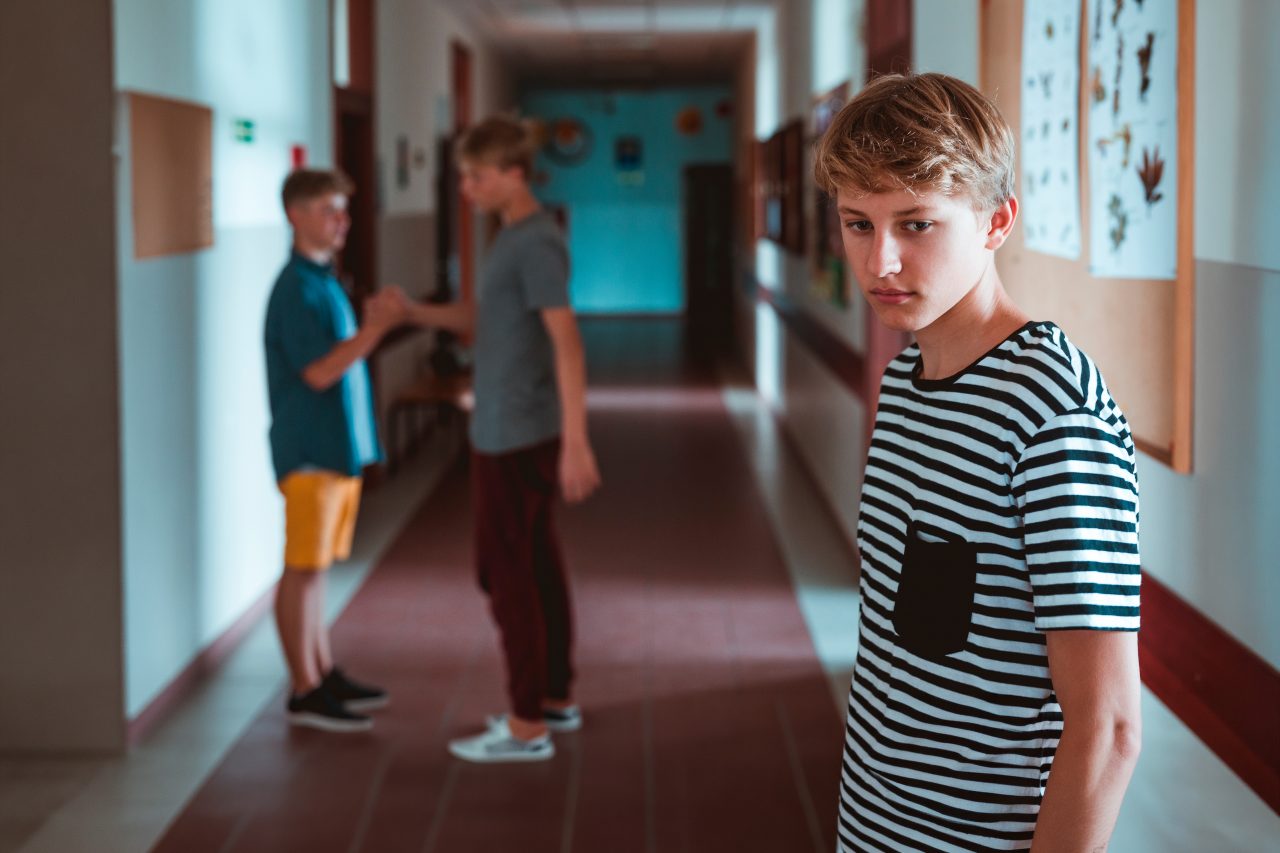 En alvorlig utseende gutt står i skolegangen. Bak ham står to klassekamerater