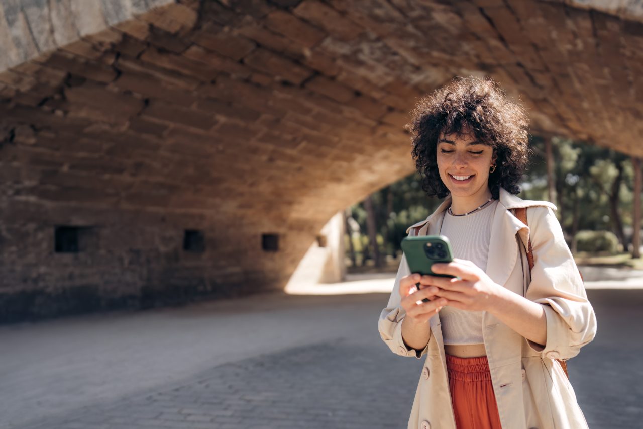 En ung person som smiler mens han holder en smarttelefon