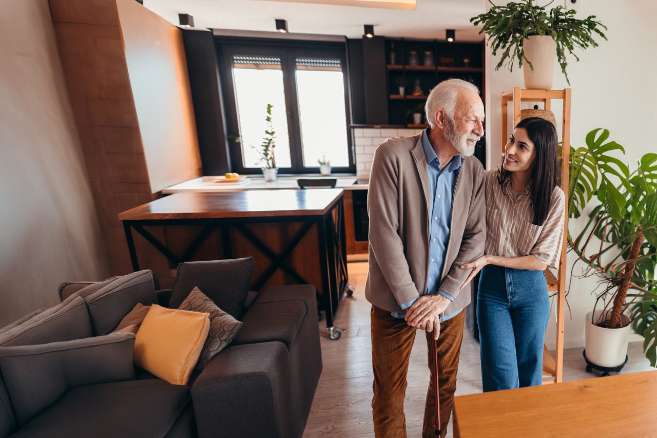 Ung kvinne som støtter en eldre mann med stokk