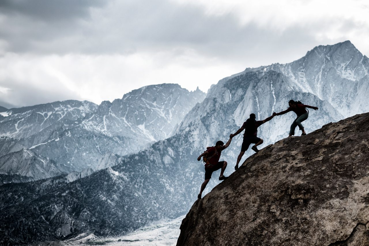 En gruppe mennesker på fjelltopp som klatrer, noe som fremmer samarbeid